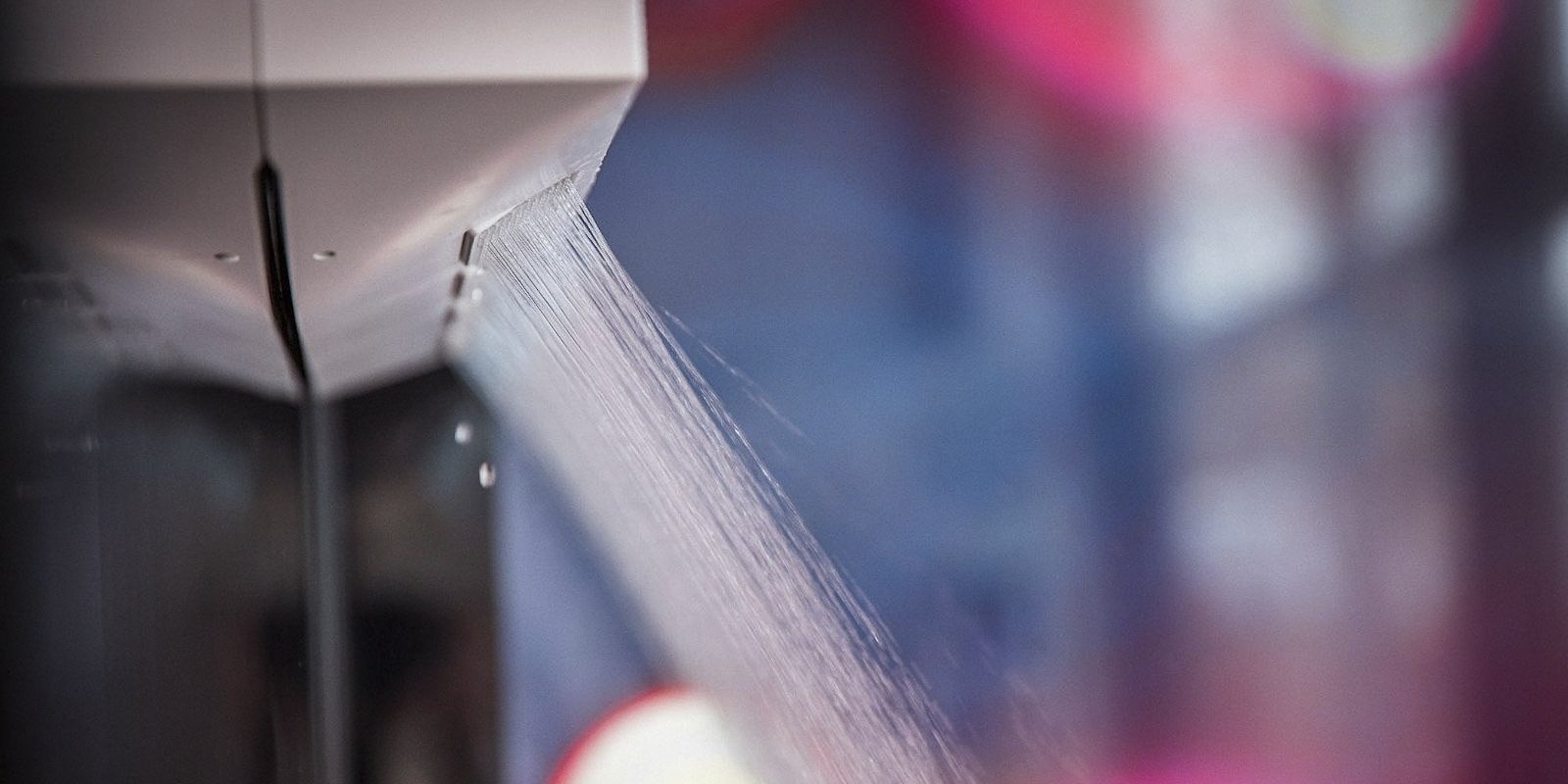 Ein Wasserstrahl spritzt aus einem modernen Wasserhahn, während der Hintergrund unscharf und farbenfroh ist.