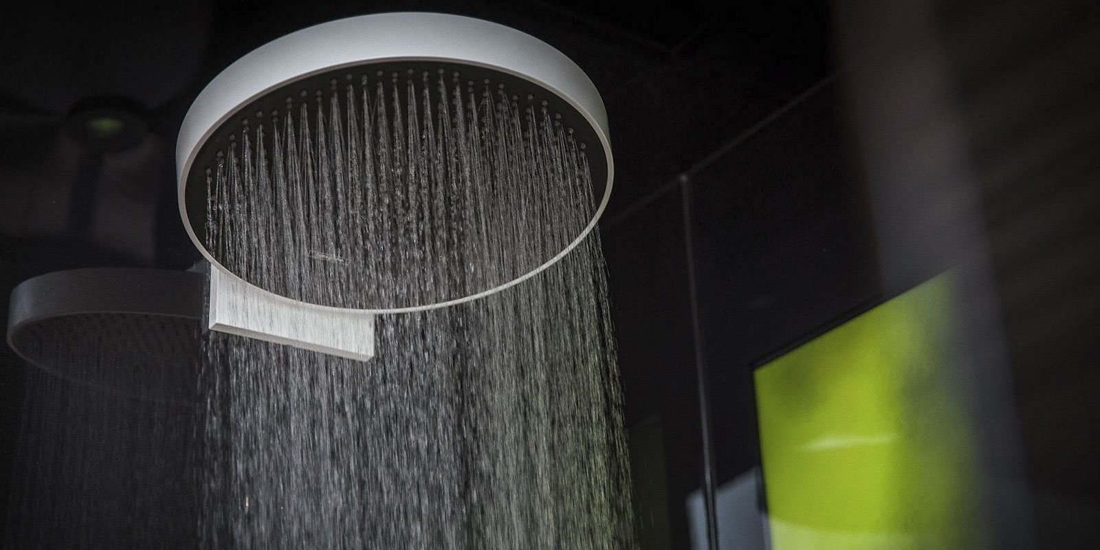 Eine moderne Regendusche mit feinen Wasserstrahlen, die sanft nach unten fließen, vor einem dunklen Hintergrund.