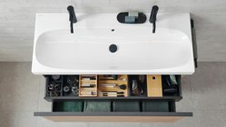 Die Badewanne ist mit zwei schwarzen Wasserhähnen ausgestattet, während der Unterbau praktische Aufbewahrung bietet.