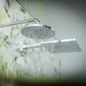 Eine moderne Duschkopf-Installation, die Wasser in feinen Strahlen abgibt, vor einem blumigen Duschvorhang.
