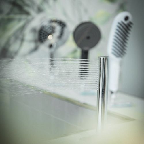 Ein moderner Wasserhahn sprudelt frisches Wasser in ein elegantes Waschbecken, während Haartrockner im Hintergrund stehen.