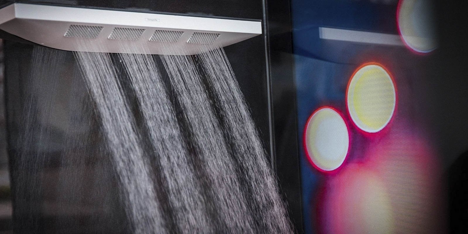 Ein moderner Duschkopf strömt Wasser in feinen Strahlen, während im Hintergrund verschwommene Lichter leuchten.
