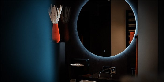 Ein modernes Badezimmer mit einem großen, beleuchteten Spiegel und einem eleganten Waschbecken, umgeben von stilvollen Dekorationen.