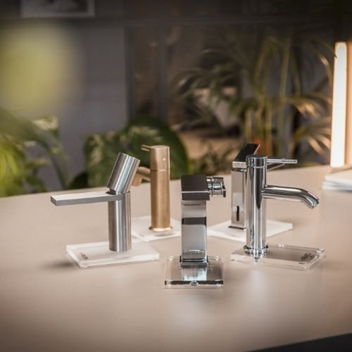 Vier moderne Wasserhähne stehen auf einem eleganten Tisch, umgeben von sanften Pflanzen im Hintergrund.