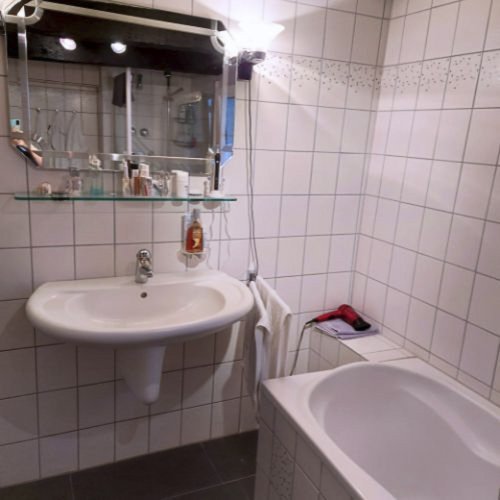 Ein modernes Badezimmer mit weißen Fliesen, einem Waschbecken und einer Badewanne, die ordentlich angeordnet sind.
