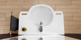 Ein modernes, weißes Waschbecken mit einem glänzenden Wasserhahn und einem gelben Drehknopf auf einem Holzfußboden.