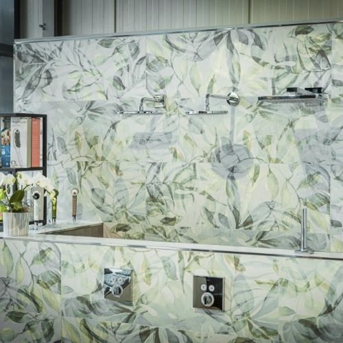 Eine moderne Badezimmerwand mit einem eleganten Blattmuster in sanften Grüntönen und glänzenden Armaturen.