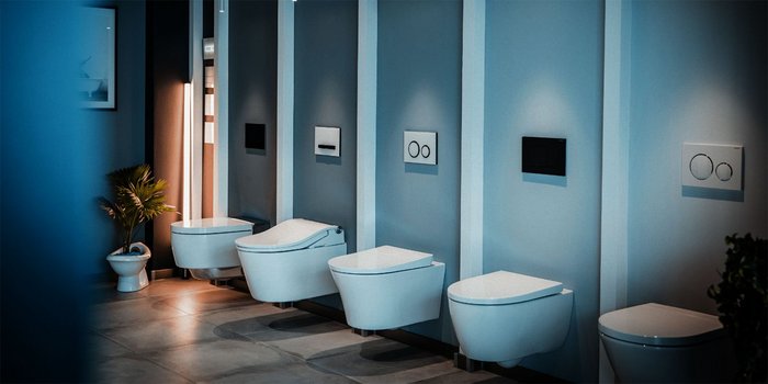 In einem schlichten Raum stehen verschiedene Toiletten nebeneinander, umgeben von sanften Lichtquellen und Pflanzen.