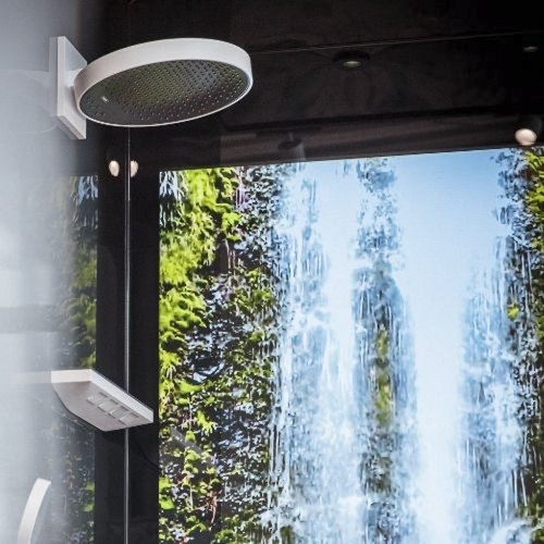 Eine moderne Dusche mit einem großen, runden Duschkopf, der über einem Wasserfall-Motiv im Hintergrund schwebt.