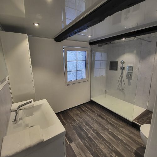 Ein modernes Badezimmer mit einer großen Dusche, einem Waschbecken und einem Fenster, das Tageslicht hereinlässt.