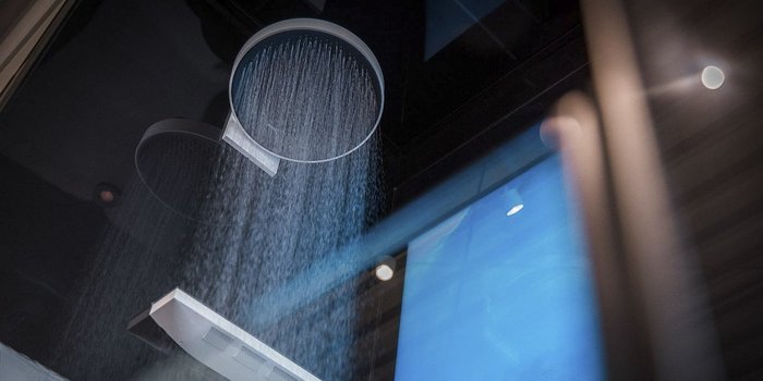 Eine moderne Dusche mit einem großen, runden Duschkopf, aus dem feines Wasser in einem eleganten Raum strömt.