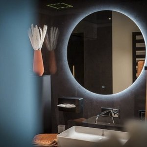 Ein modernes Badezimmer mit einem runden Spiegel, der sanft beleuchtet ist, und einem eleganten Waschbecken im Vordergrund.