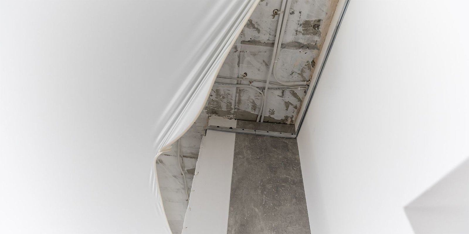 Ein Blick auf eine schlichte, weiße Wand mit einem abgehängten Deckenbereich, der unvollständig aussieht.