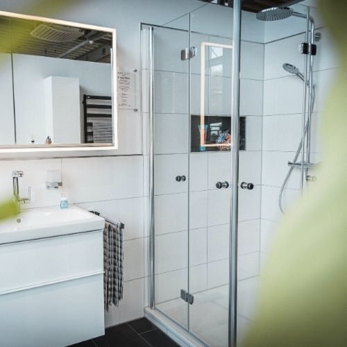 Ein modernes Badezimmer mit einer gläsernen Dusche und einem eleganten Waschbecken, umgeben von hellen Fliesen.