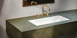 Ein elegantes Waschbecken aus weißem Keramik, umgeben von einer grünen Steinplatte und goldenen Wasserhähnen.
