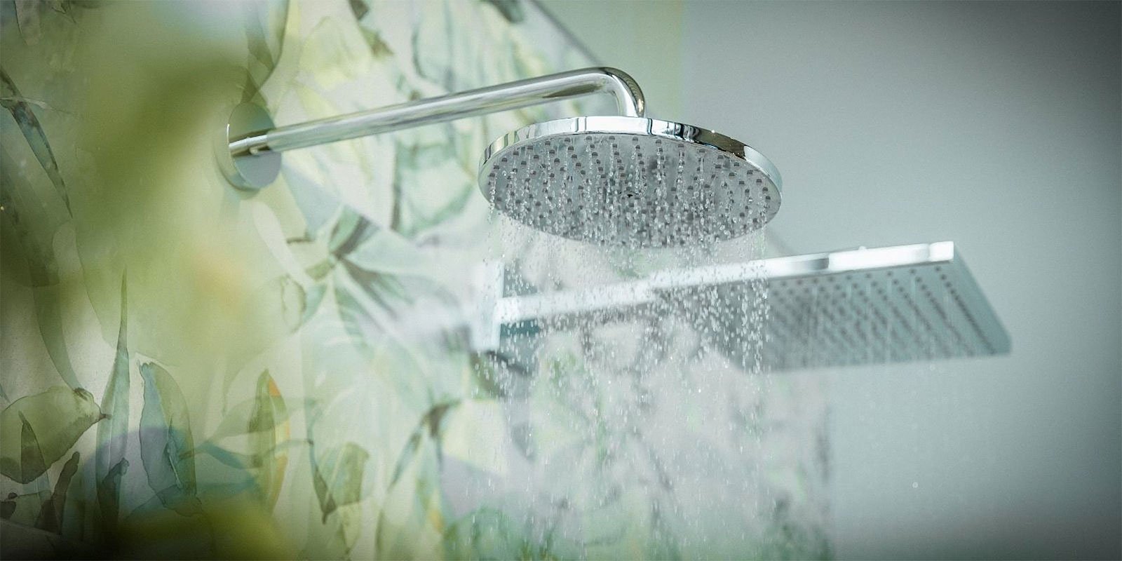 Der glänzende Duschkopf gibt einen feinen Wasserstrahl ab, während die sanften Farben der Wand im Hintergrund sichtbar sind.