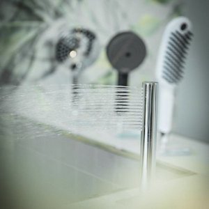 Ein moderner Wasserhahn sprudelt frisches Wasser in einem eleganten Badezimmer mit stilvollen Haartrocknern im Hintergrund.