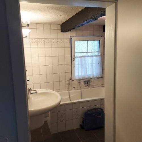 Ein helles Badezimmer mit einer Badewanne, einem Waschbecken und einem Fenster, das Tageslicht hereinlässt.