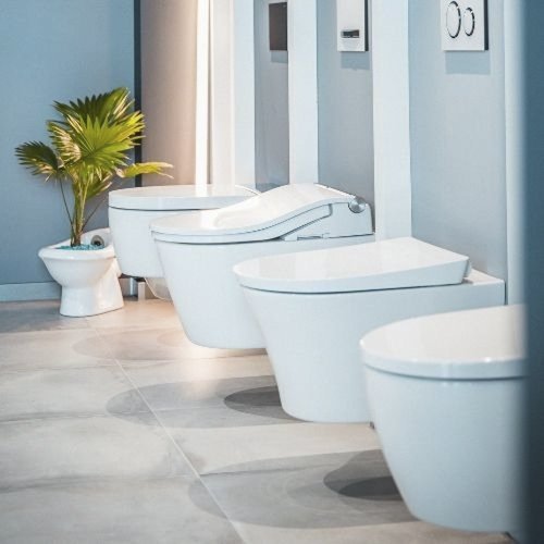 In einem modernen Badezimmer stehen mehrere elegante Toiletten nebeneinander, ergänzt durch eine grüne Pflanze in der Ecke.